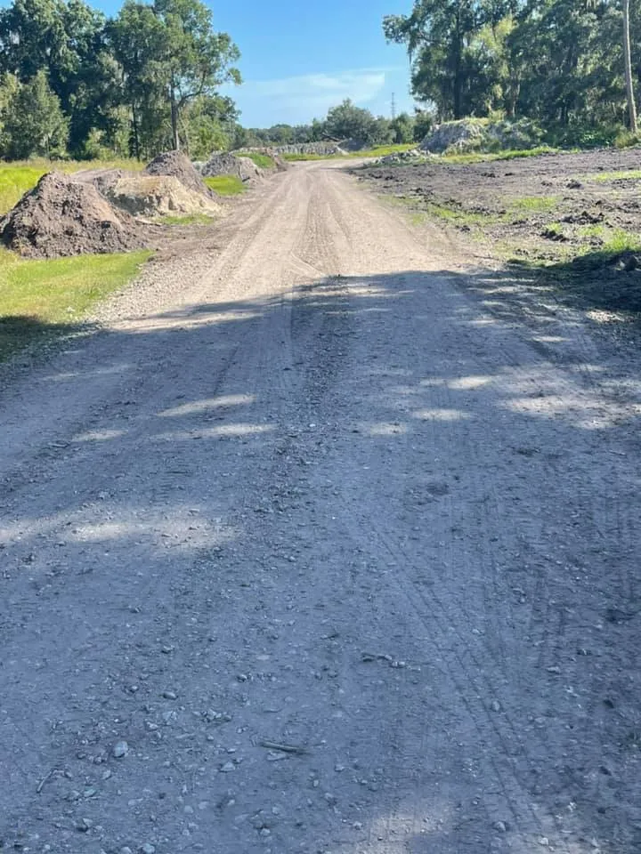 Graded gravel drive cut between live oaks, with dirt piles along the edge, Bartow, FL area